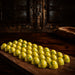 A row of small, glossy yellow confectionery Chocolate bon bons yuzu flavor with green speckles arranged on a dark wooden board in a rustic, dimly lit setting.